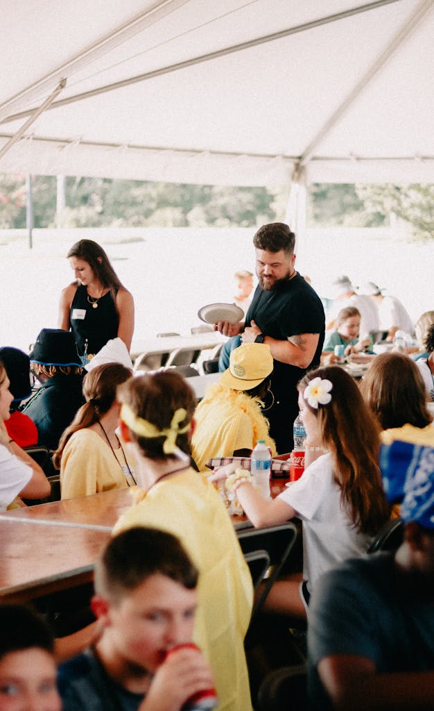 Joyful outdoor gathering of a diverse church community sharing a meal under a tent.