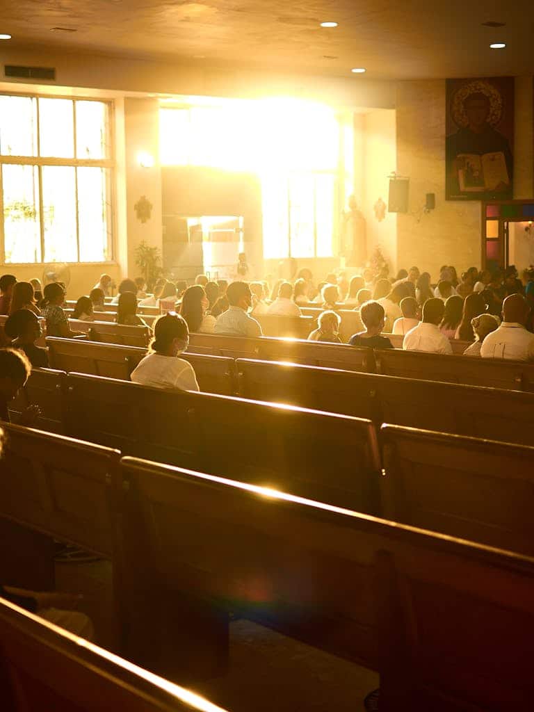 Sunlit church interior filled with people during a service, highlighting a serene religious atmosphere.