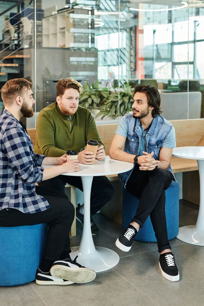Three diverse coworkers engaged in a casual discussion in a modern office setting.